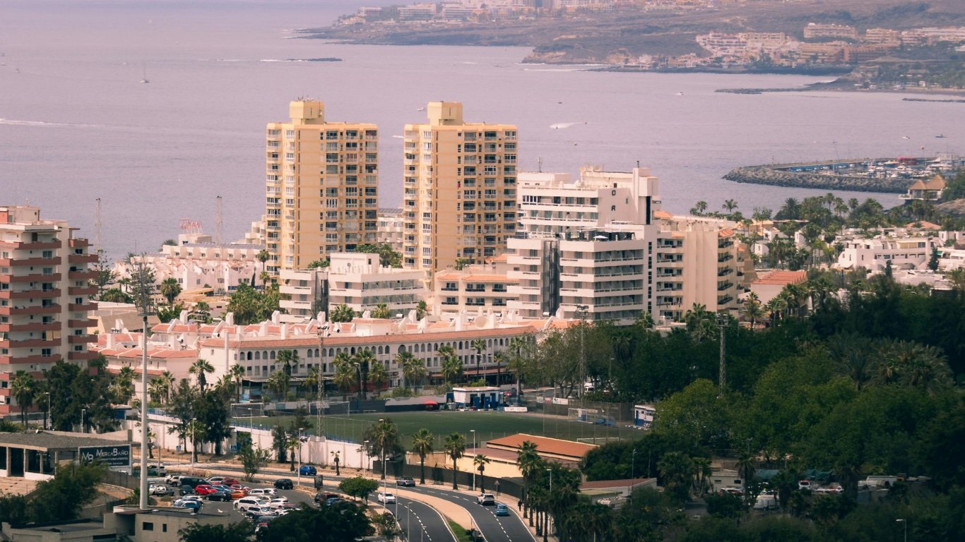 Vista elevada de una urbanización turística junto al mar, con dos torres de apartamentos, hoteles y bloques de baja altura frente a la costa